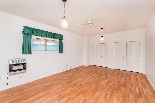 unfurnished bedroom with heating unit, light wood finished floors, multiple closets, and baseboards