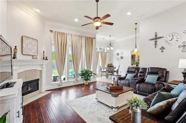 living room with a ceiling fan, hardwood / wood-style floors, a tiled fireplace, ornamental molding, and recessed lighting