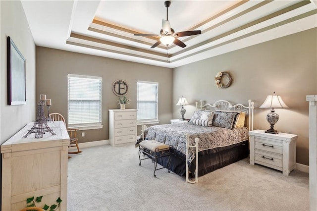 bedroom with a raised ceiling, light colored carpet, baseboards, and ceiling fan