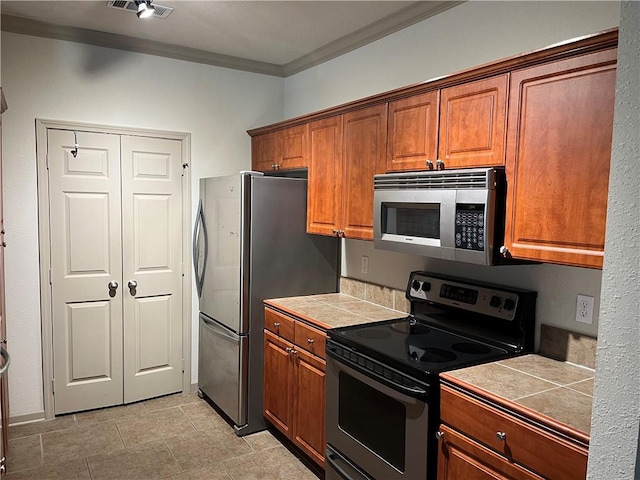 kitchen featuring stainless steel appliances, crown molding, tile countertops, and brown cabinets