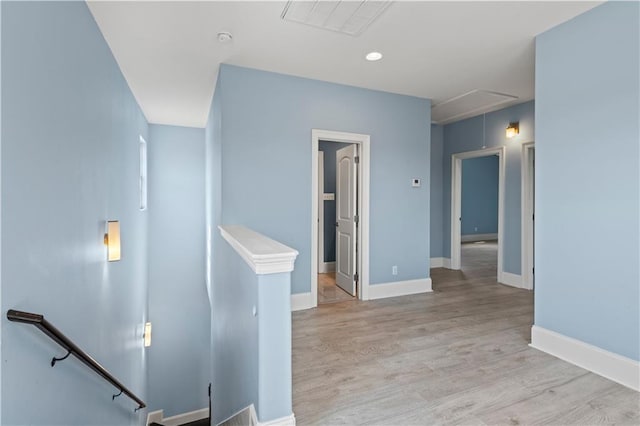 hallway with an upstairs landing, attic access, light wood-style floors, and baseboards