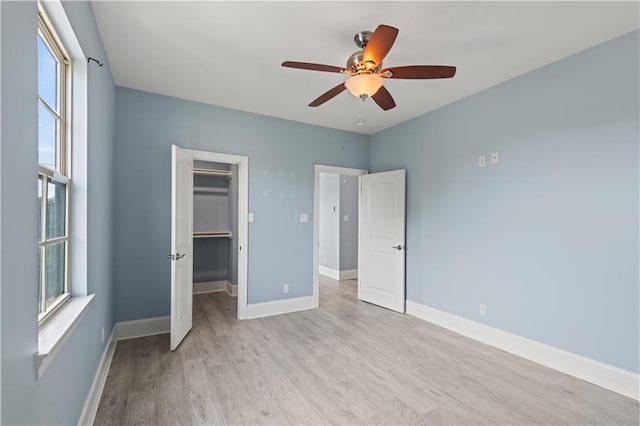 unfurnished bedroom with light wood-style floors, a walk in closet, baseboards, a ceiling fan, and a closet