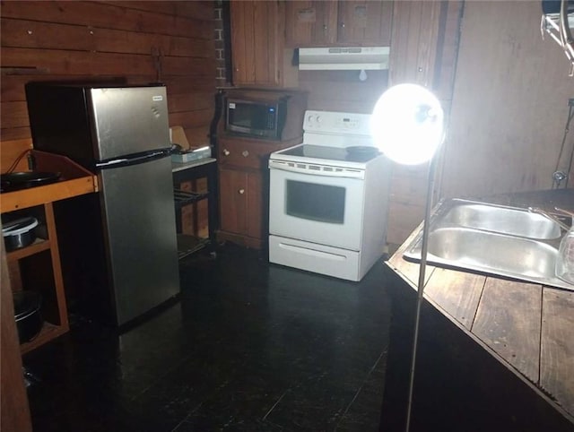 kitchen with stainless steel appliances, under cabinet range hood, a sink, brown cabinetry, and wooden walls