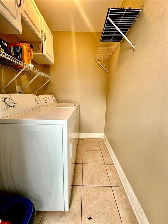 clothes washing area with washing machine and clothes dryer, cabinet space, light tile patterned floors, and baseboards