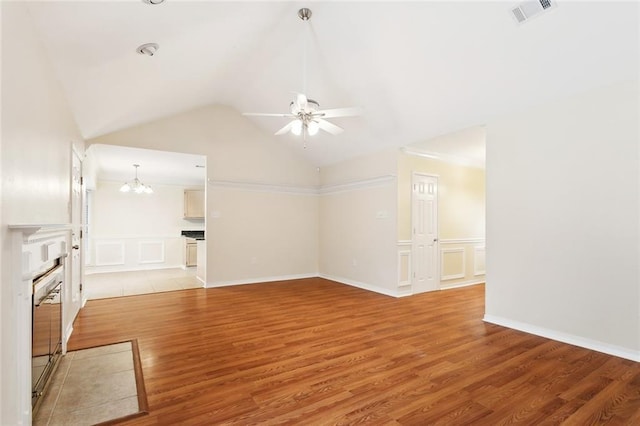 unfurnished living room featuring a decorative wall, a ceiling fan, light wood finished floors, wainscoting, and vaulted ceiling