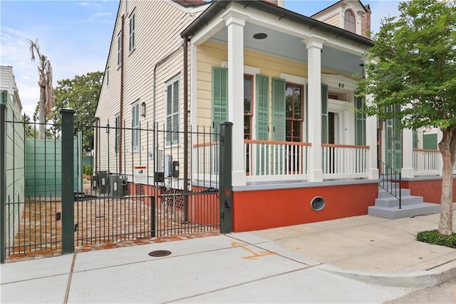 view of property exterior with covered porch, fence, and a gate