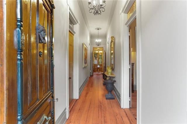 hallway featuring a chandelier, light wood finished floors, and crown molding