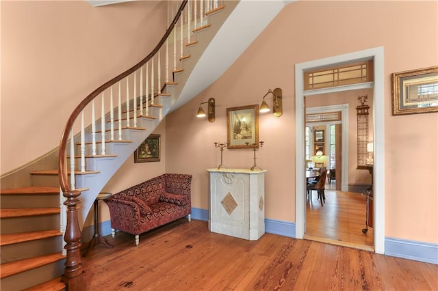 staircase with wood finished floors, baseboards, and a towering ceiling