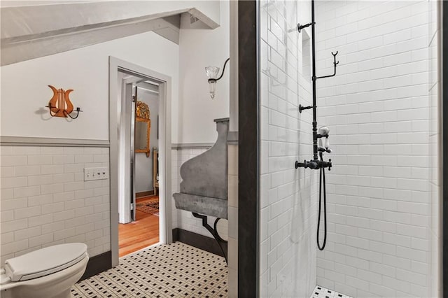 full bathroom with tile walls, wainscoting, a tile shower, and toilet