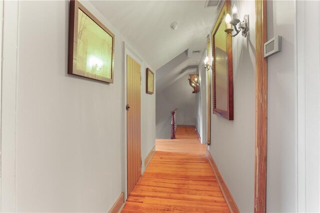 hallway with light wood-type flooring, vaulted ceiling, and baseboards