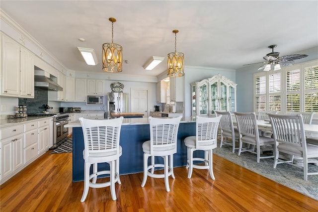228 Marlin Dr, Slidell, LA 70461 - kitchen with stainless steel appliances, a chandelier, wall chimney range hood, wood finished floors, and white cabinetry