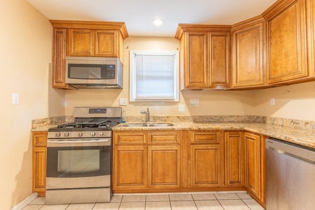 kitchen with stainless steel appliances, a sink, brown cabinets, light stone counters, and recessed lighting