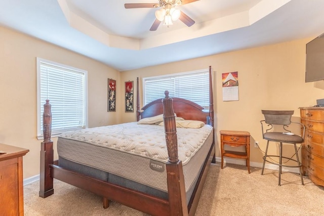 bedroom with a raised ceiling, light carpet, baseboards, and ceiling fan