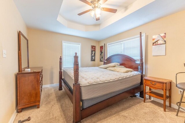 bedroom with light carpet, baseboards, a tray ceiling, and a ceiling fan
