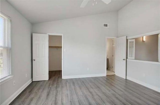 unfurnished bedroom featuring wood finished floors, a walk in closet, high vaulted ceiling, a ceiling fan, and baseboards