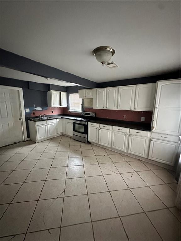 kitchen with stainless steel range with electric cooktop, dark countertops, light tile patterned flooring, and white cabinets