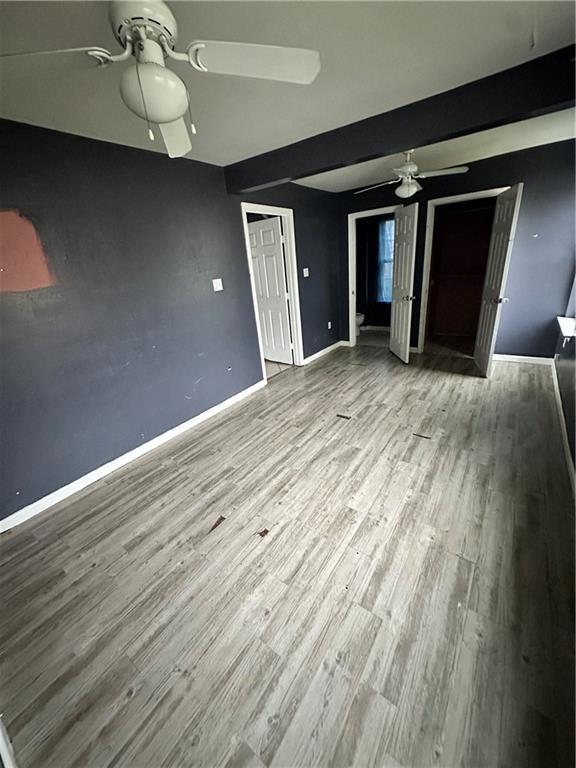 unfurnished living room with a ceiling fan, wood finished floors, and baseboards