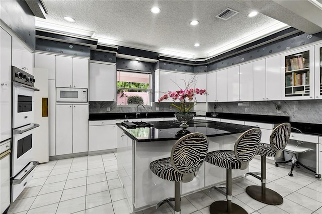 3805 3rd St, Metairie, LA 70002 - kitchen with a textured ceiling, white appliances, dark countertops, white cabinetry, and a breakfast bar area
