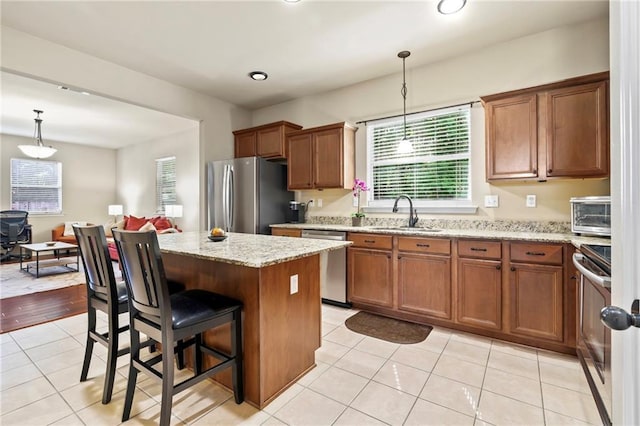 kitchen with appliances with stainless steel finishes, brown cabinetry, a sink, light tile patterned flooring, and a kitchen island