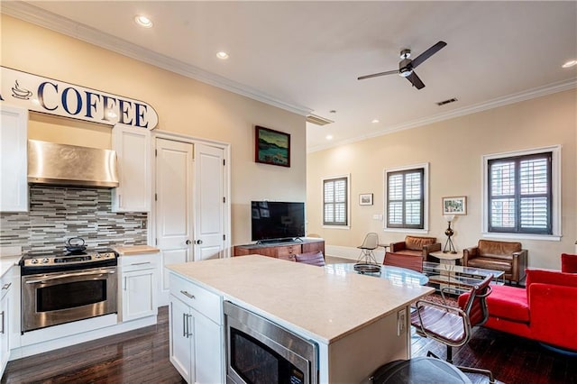 kitchen featuring stainless steel appliances, wall chimney range hood, open floor plan, dark wood-type flooring, and ceiling fan