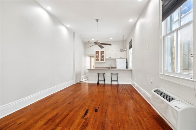 unfurnished living room featuring wood finished floors, a wall mounted AC, recessed lighting, baseboards, and a ceiling fan