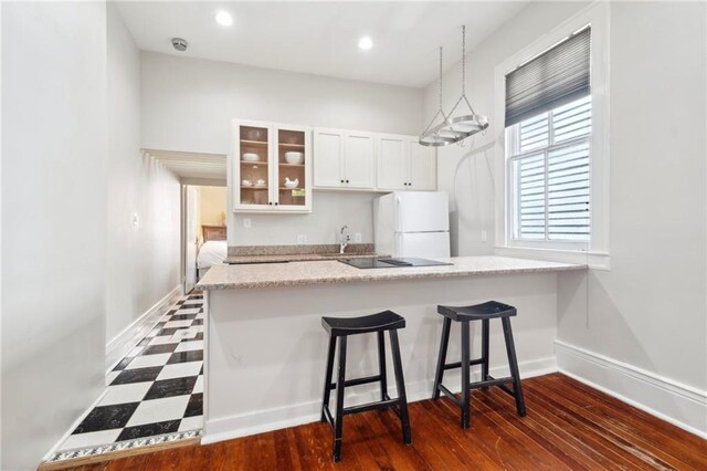 kitchen with freestanding refrigerator, a breakfast bar area, glass insert cabinets, white cabinetry, and a sink