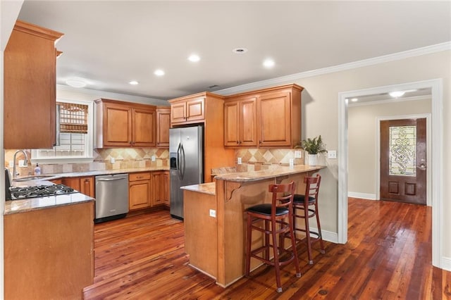 kitchen featuring stainless steel appliances, a sink, healthy amount of natural light, a peninsula, and ornamental molding