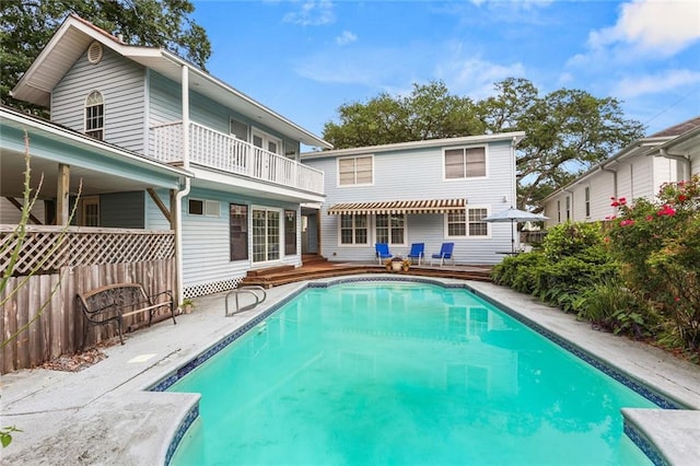 rear view of house featuring an outdoor pool, a balcony, fence, and a wooden deck