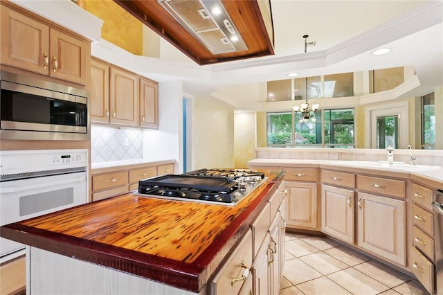 1306 Woodmere Dr, Mandeville, LA 70471 - kitchen with wood counters, appliances with stainless steel finishes, a tray ceiling, light brown cabinetry, and a center island