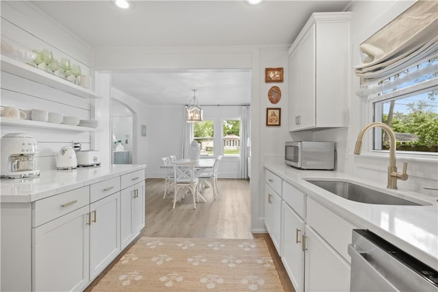kitchen with appliances with stainless steel finishes, a sink, white cabinets, light countertops, and light wood-type flooring