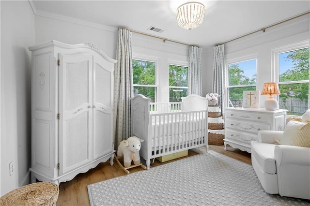 bedroom featuring wood finished floors, a nursery area, and a chandelier