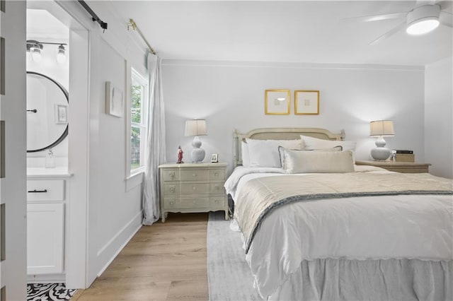 bedroom with light wood-type flooring, a ceiling fan, a barn door, crown molding, and baseboards