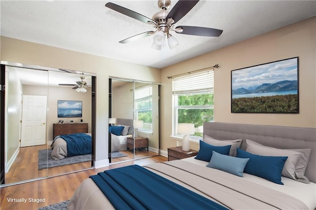 bedroom featuring two closets, wood finished floors, a textured ceiling, a ceiling fan, and baseboards