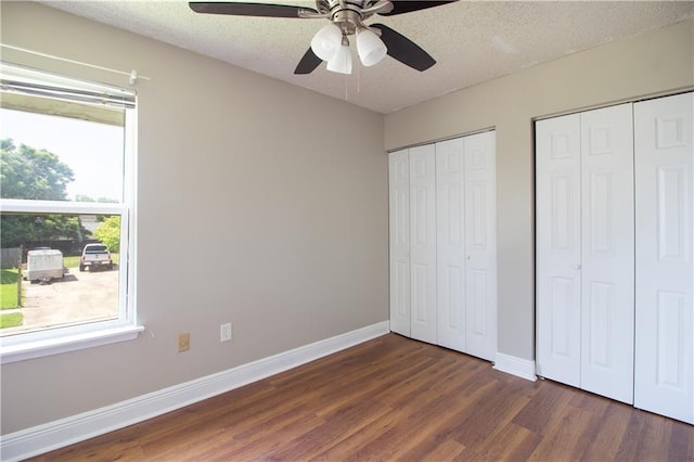 unfurnished bedroom featuring wood finished floors, multiple closets, baseboards, a textured ceiling, and ceiling fan