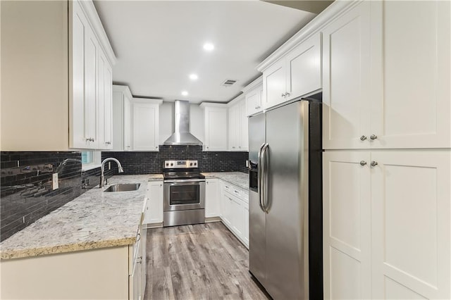 kitchen with appliances with stainless steel finishes, wall chimney range hood, a sink, decorative backsplash, and recessed lighting