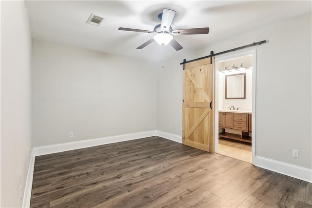 unfurnished bedroom featuring a barn door, wood finished floors, baseboards, and a sink