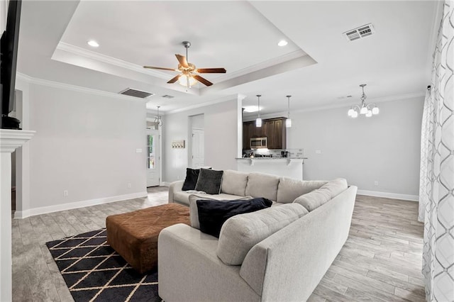 living room featuring ceiling fan, a tray ceiling, light wood finished floors, recessed lighting, and a chandelier