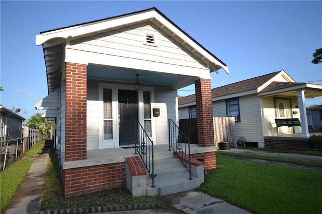 shotgun-style home featuring a porch, brick siding, and fence