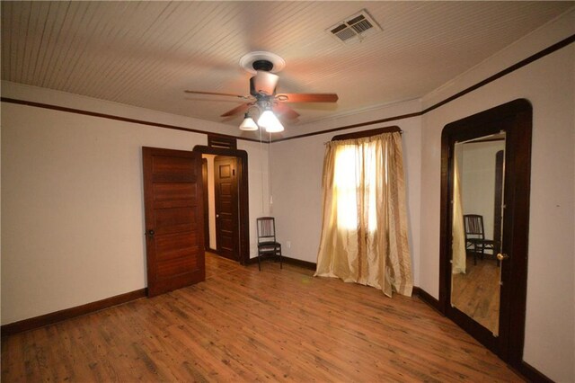 unfurnished bedroom featuring baseboards, wood finished floors, crown molding, and a ceiling fan