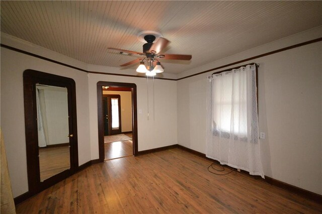 unfurnished room featuring healthy amount of natural light, wood finished floors, a ceiling fan, baseboards, and crown molding