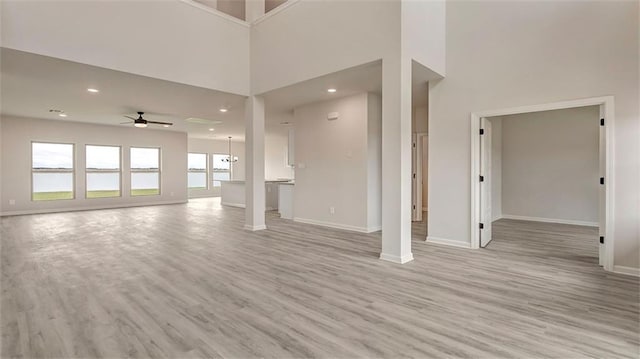 unfurnished living room featuring a ceiling fan, baseboards, light wood-style floors, recessed lighting, and a towering ceiling