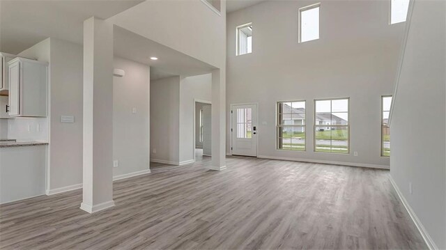 unfurnished living room with light wood finished floors, a high ceiling, and baseboards