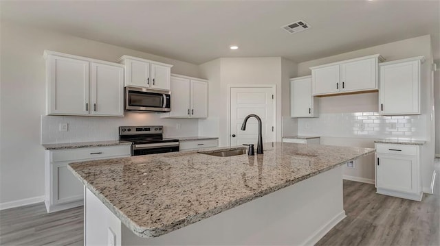 kitchen featuring appliances with stainless steel finishes, a sink, an island with sink, light stone countertops, and white cabinetry