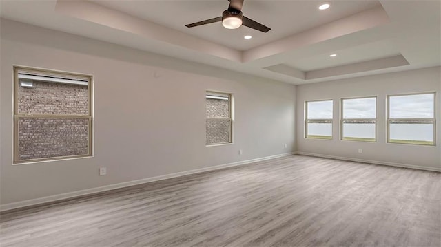 empty room featuring a tray ceiling, wood finished floors, ceiling fan, baseboards, and recessed lighting