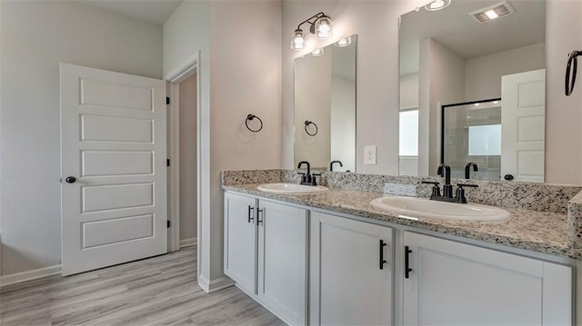 bathroom featuring a stall shower, wood finished floors, double vanity, and baseboards