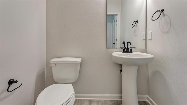 half bath featuring toilet, baseboards, and a sink