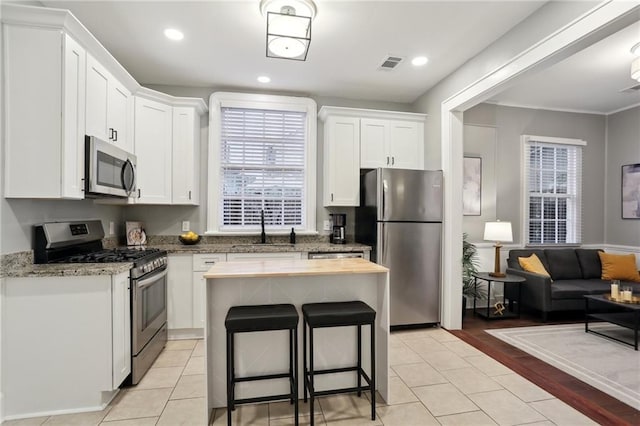 724 Port St, New Orleans, LA 70117 - kitchen with stainless steel appliances, a sink, white cabinetry, a kitchen bar, and light tile patterned floors