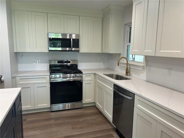 kitchen featuring stainless steel appliances, a sink, white cabinetry, light stone counters, and dark wood finished floors