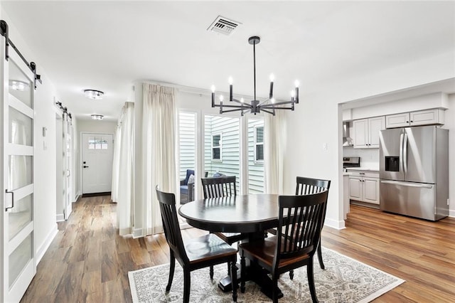 dining room featuring a barn door, a chandelier, light wood-type flooring, and baseboards
