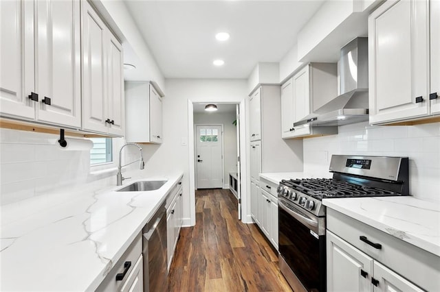 kitchen featuring appliances with stainless steel finishes, wall chimney exhaust hood, a sink, dark wood-style flooring, and backsplash